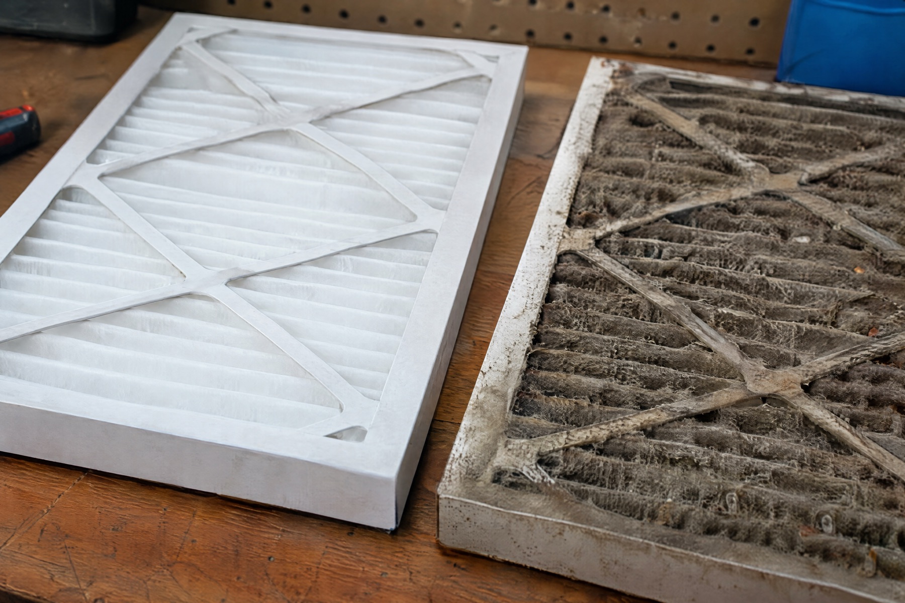 A clean white pleated air filter next to a grey, dust-clogged filter on a wooden workbench