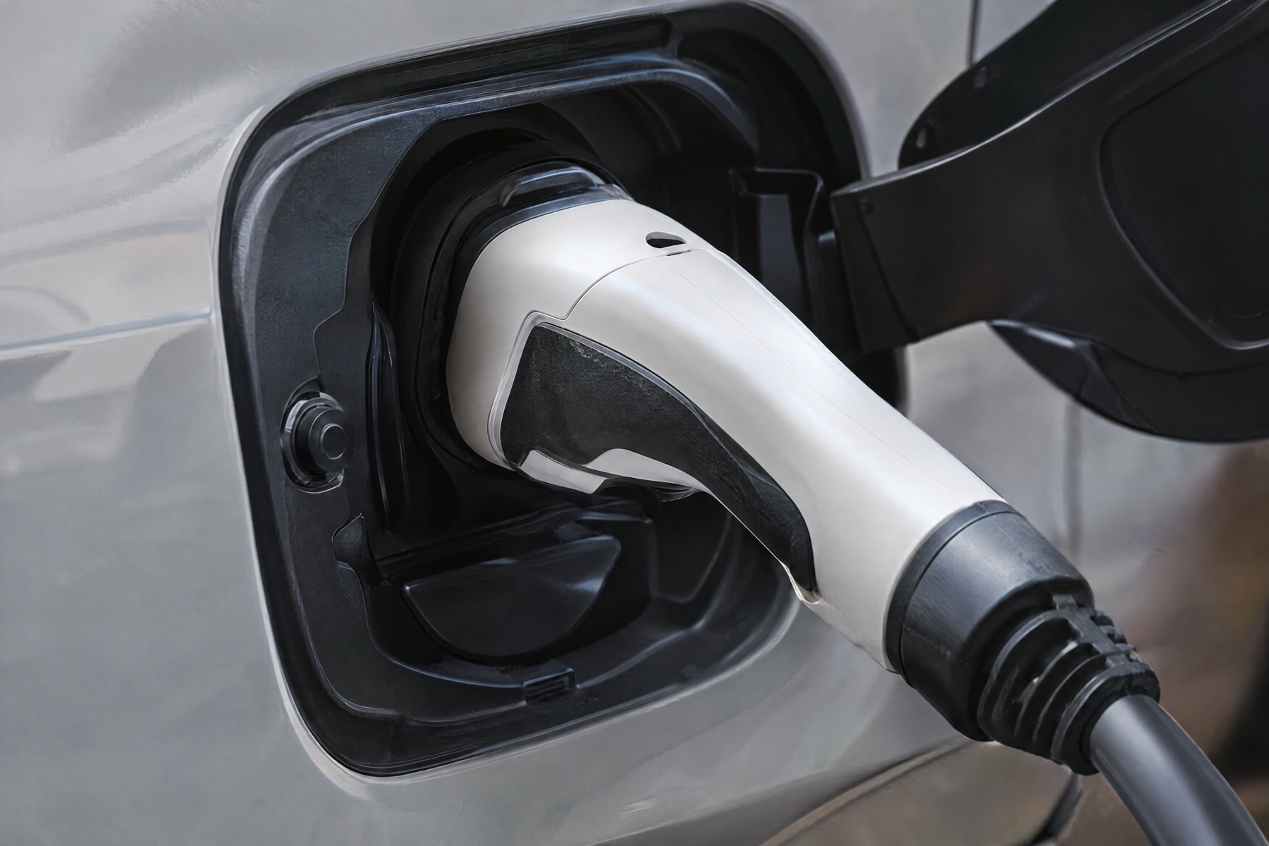A white Level 2 charging connector plugged into the charge port of a silver electric car