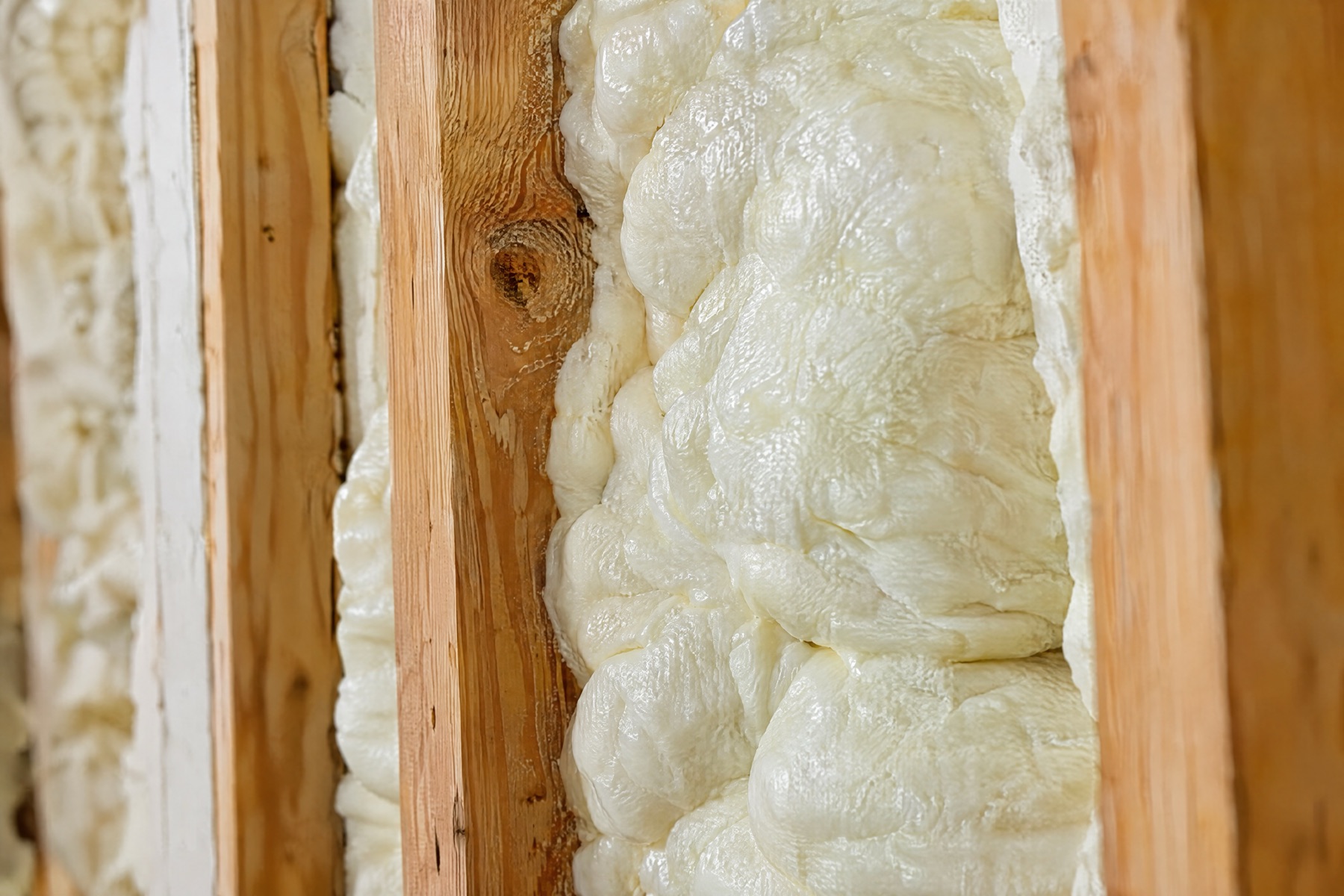 Cream-coloured spray-foam insulation expanded between wooden wall studs