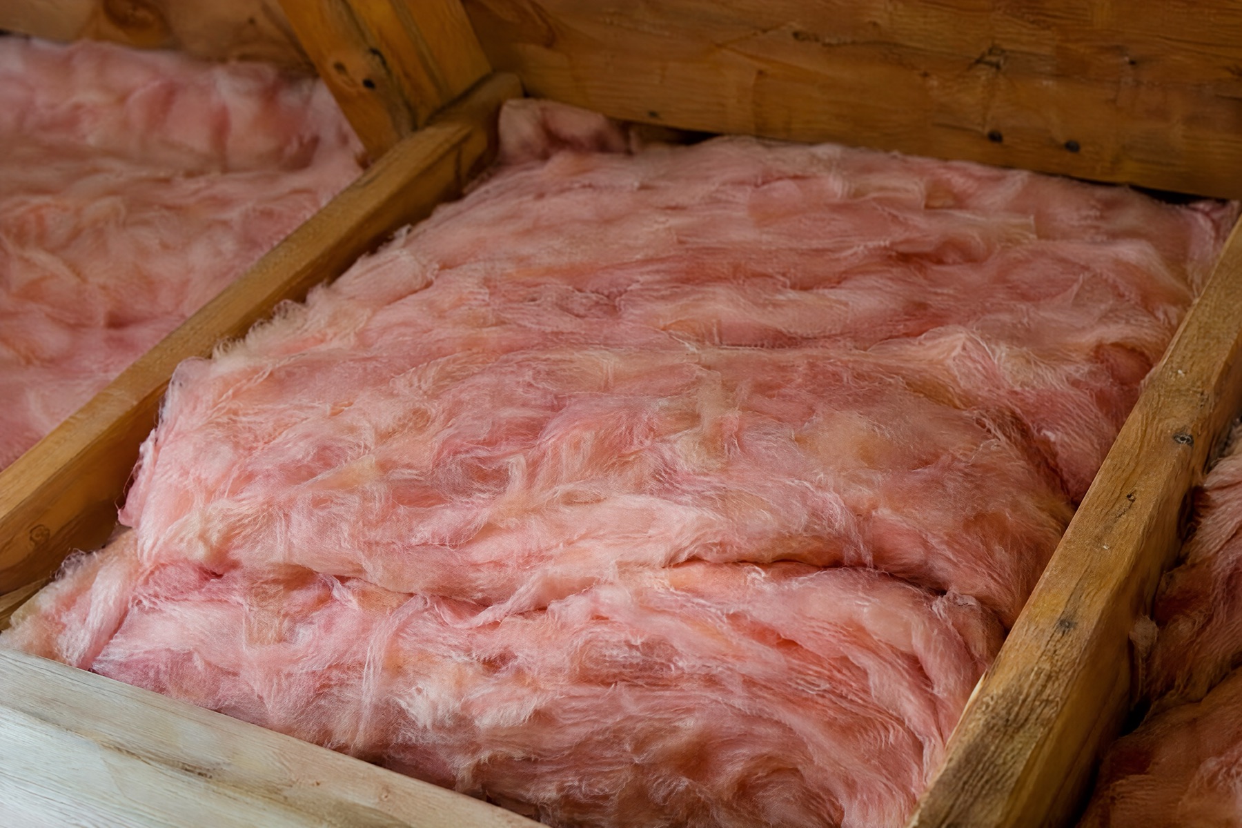Pink fiberglass insulation batts laid snugly between wooden attic joists