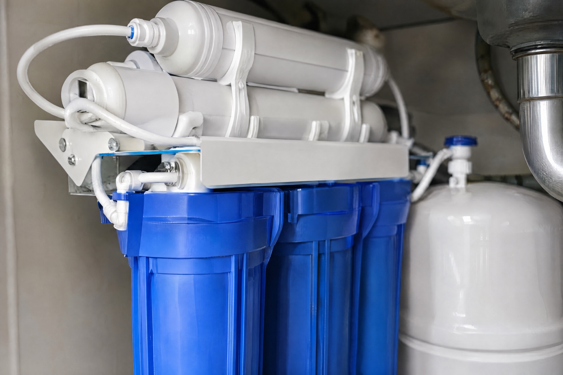 An under-sink reverse-osmosis filter system with blue filter housings and a white storage tank