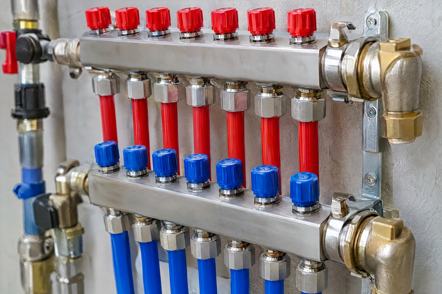 A stainless radiant-floor manifold with rows of red and blue valve caps and matching PEX loops